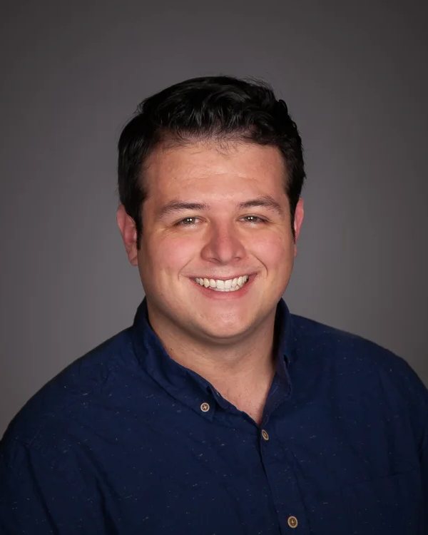 Riley, smiling, in a navy button-up shirt